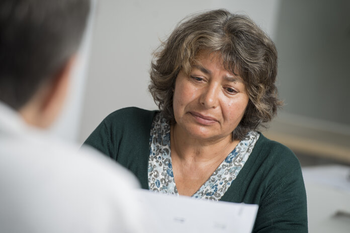 Eine Frau sitzt vor einem Arzt, erfährt ihren Befund und sieht nicht glücklich aus.