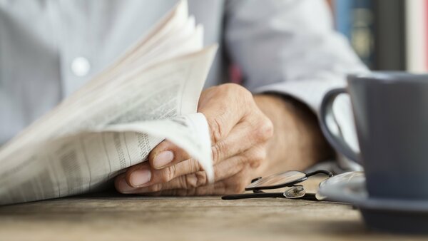 Mann sitzt mit Kaffeetasse am Tisch und liest Zeitung