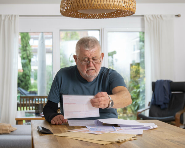 Ein älterer Herr sitzt am Esstisch und ordnet Unterlagen.