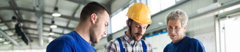 Drei Männer besprechen sich bei der Arbeit in einer Lagerhalle.