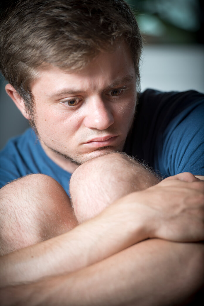 Junger Mann sitzt traurig schauend auf dem Sofa.