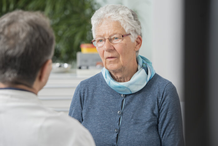 Eine ältere Patientin mit nachdenklichem Blick ist im Beratungsgespräch mit einem Mediziner in der Arztpraxis.