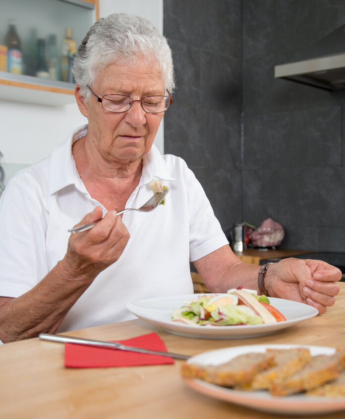 Ältere Frau sitzt am Esstisch und hat keinen Apetit beim Essen.