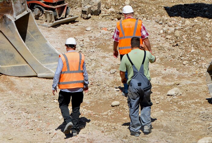 3 Bauarbeiter gehen bei Sonnenschein über eine Baustelle