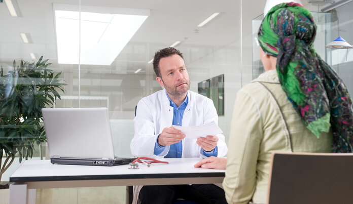 Arzt und Patientin sitzen an einem Tisch und führen ein Gespräch.