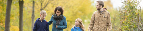 Eine junge Frau und ein junger Mann gehen mit einem Mädchen und einem Jungen im Park spazieren unter unterhalten sich ernst.