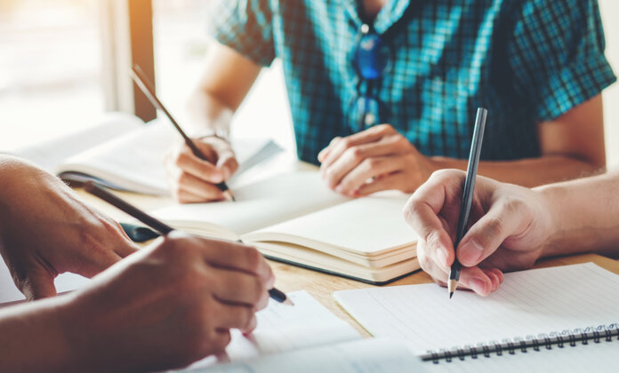 Schüler sitzen an einem Tisch mit ihren Schreibblöcken und Stiften in der Hand.