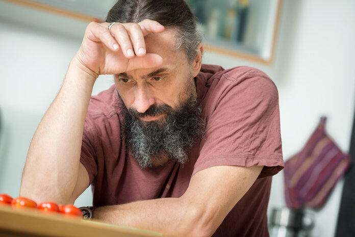 Mann sitzt am Tisch und stützt sich den Kopf.