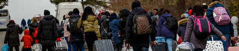 Eine Gruppe ukrainischer Flüchtlinge mit Gepäck und Rollkoffern geht eine Straße entlang