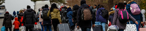 Eine Gruppe ukrainischer Flüchtlinge mit Gepäck und Rollkoffern geht eine Straße entlang