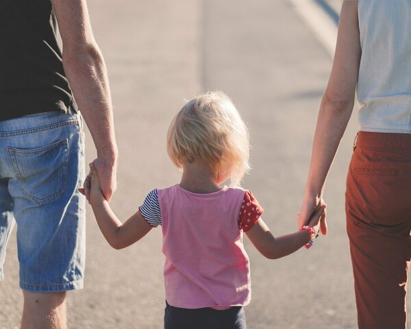 Ein kleines Kind läuft Hand in Hand mit seinen Eltern.