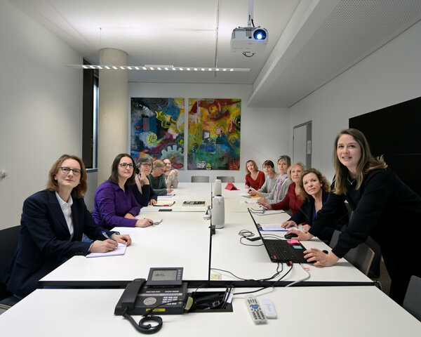 Mitarbeiterinnen des Krebsinformationsdienstes sitzen an einem Besprechungstisch und hören bei einer Präsentation einer Kollegin zu.