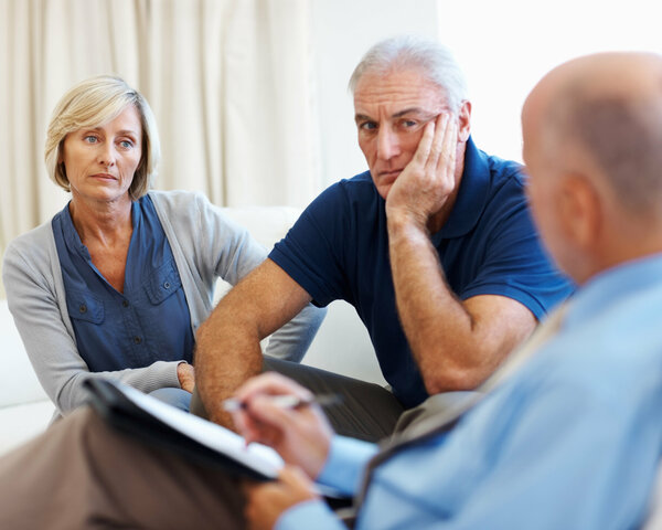 Älteres Ehepaar sitzt auf einer Couch und spricht mit einem Psychologen.