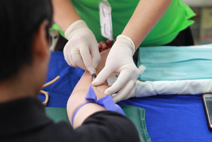 Jemand nimmt einem Patienten Blut an der Armbeuge ab.