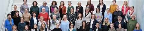 Mitarbeitende des krebsinformationsdienst stehen gruppiert zu einem Teamfoto auf einer Treppe