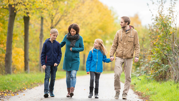 Mutter und Vater gehen mit ihren zwei Kindern im herbstlichen Park spazieren und sprechen intensiv miteinander.