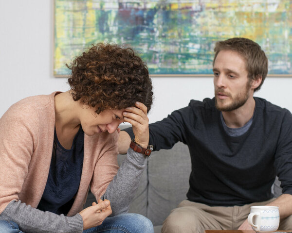 Junge Frau und ihr Partner unterhalten sich auf einem Sofa.