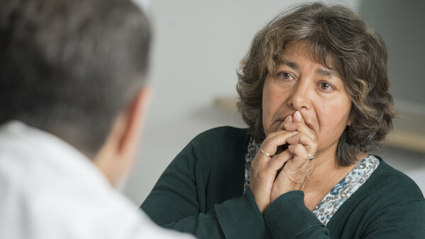 Patientin hält ihre Hände vor den Mund, während sie mit ihrem Arzt ihre Diagnose bespricht.