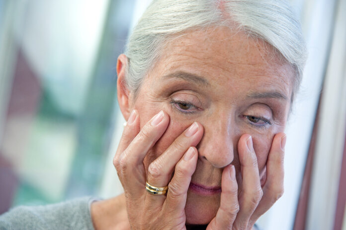 Eine Frau mit müden und besorgtem Blick legt die Hände um ihr Gesicht.