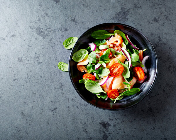 Salat mit Tomaten und Lachs auf grauem Tisch