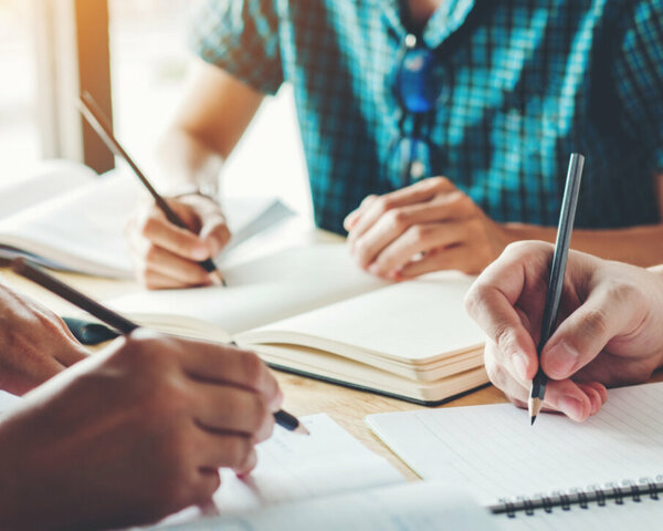 Schüler sitzen an einem Tisch mit ihren Schreibblöcken und Stiften in der Hand.