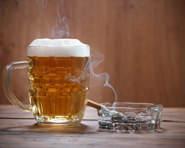 Volles Bierglas steht auf einem Tisch neben einem Aschenbecher mit einer qualmenden Zigarette